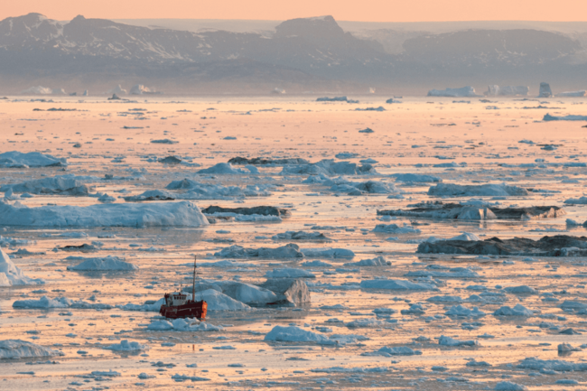 Disko Bay in sunset with a small boat amongst the ice