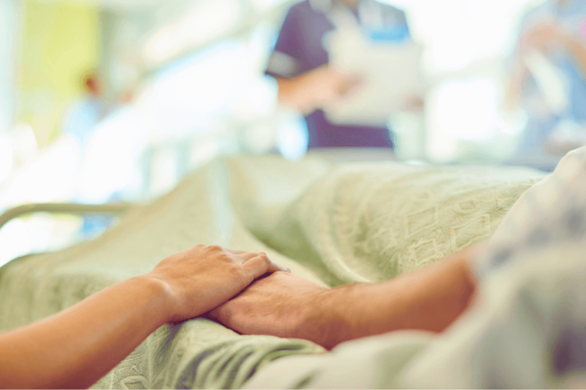 Photograph of two people holding hands in a hospital bed