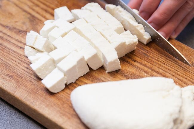 Cheese is cut into cubes on a wooden cutting board