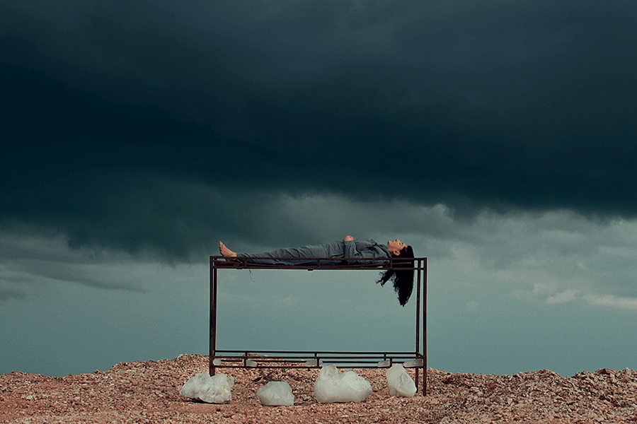 A photo of one of Marina Abramović's works, in which she is lying on a stand in a desolate place under a dark sky