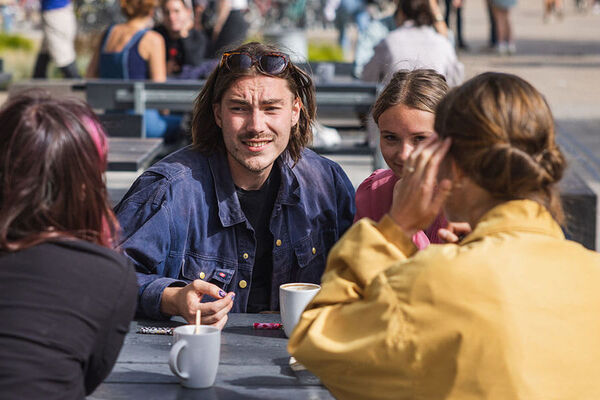 En flok glade studerende sidder ved et bord udenfor og taler grinende sammen