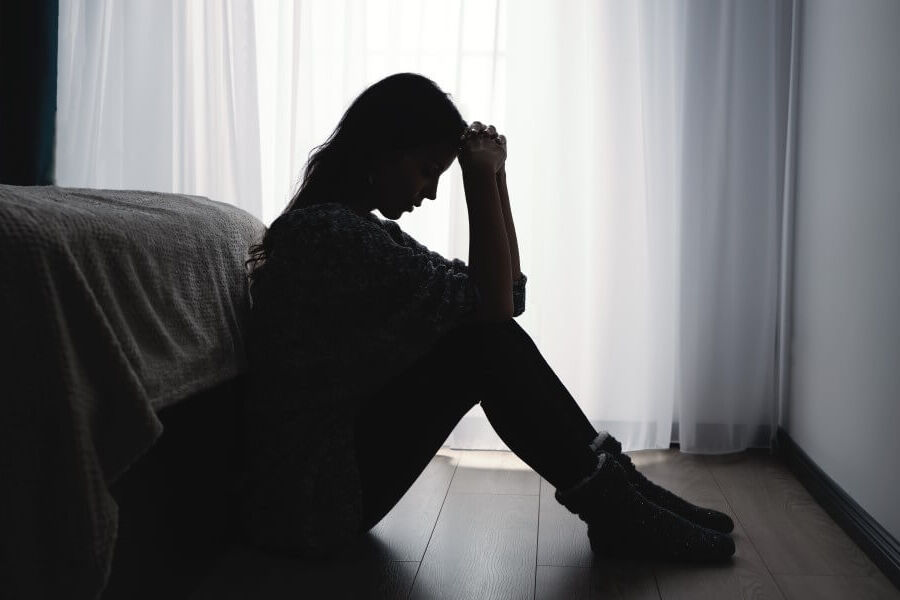 A woman is sitting at the foot of the bed in a dark room