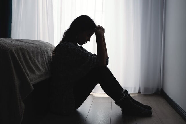 A woman is sitting at the foot of the bed in a dark room